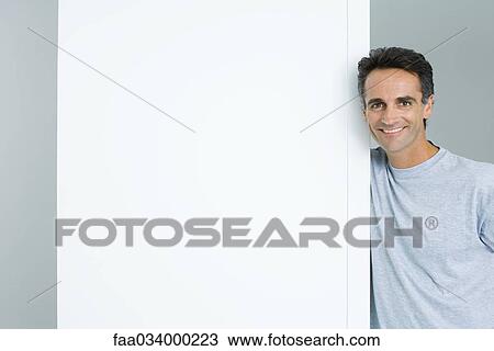 Stock Image - Man leaning against doorway, smiling at camera. Fotosearch
