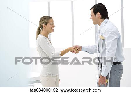 Stock Image - Man on crutches shaking woman's hand, side view. Fotosearch