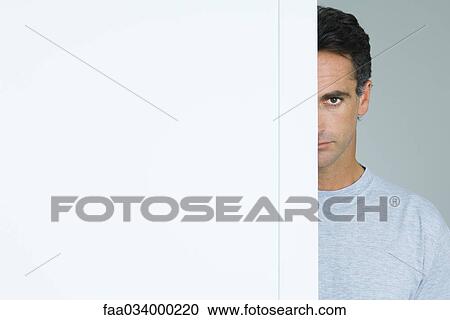 Stock Image - Man peeking around doorway at camera, cropped. Fotosearch