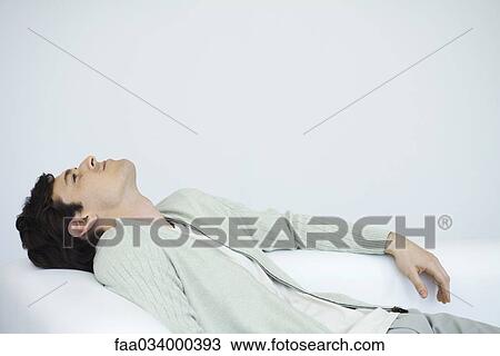 Stock Image - Man reclining on sofa, looking up. Fotosearch