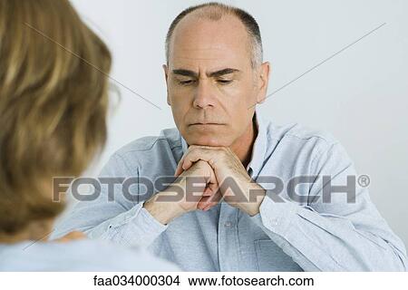 Picture - Man resting chin on clasped hands, looking down, over the shoulder view. Fotosearch