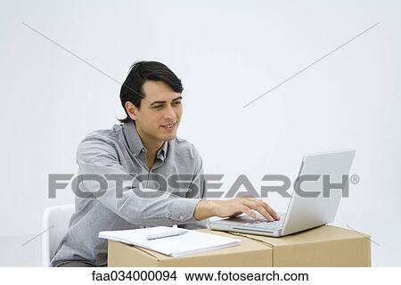 Man sitting at cardboard box desk, using laptop computer View Large Photo Image Picture - Man sitting at cardboard box desk, using laptop computer. Fotosearch