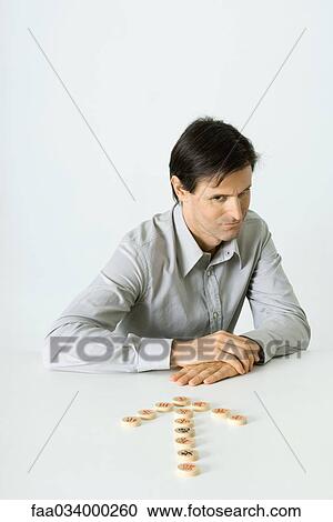 Stock Image - Man sitting before arrow made of mahjong tiles, looking down. Fotosearch