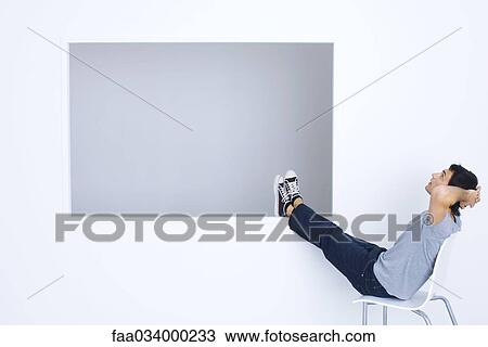 Man sitting in chair with hands behind head and legs up, looking up View Large Photo Image Stock Image - Man sitting in chair with hands behind head and legs up, looking up. Fotosearch