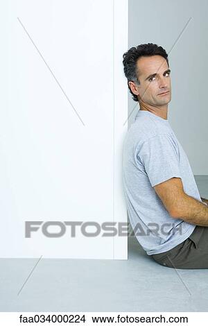 Picture - Man sitting on the ground, leaning against doorway, looking over shoulder at camera. Fotosearch