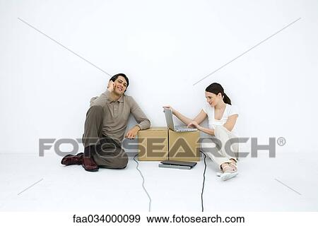 Man talking on phone, sitting on floor next to woman using laptop computer at cardboard box desk View Large Photo Image Stock Photo - Man talking on phone, sitting on floor next to woman using laptop computer at cardboard box desk. Fotosearch