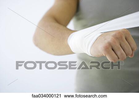 Stock Image - Man wrapping bandage around wrist, cropped view. Fotosearch