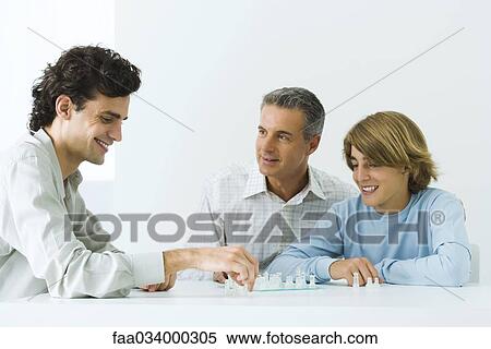 Stock Photography - Mature father and two sons playing chess, all smiling. Fotosearch