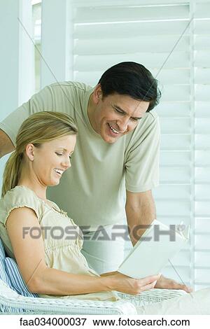 Stock Photo - Mature man and young woman reading book together, both smiling. Fotosearch