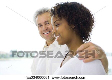 Mature man with arm around young woman's shoulder, both smiling View Large Photo Image Stock Image - Mature man with arm around young woman's shoulder, both smiling. Fotosearch