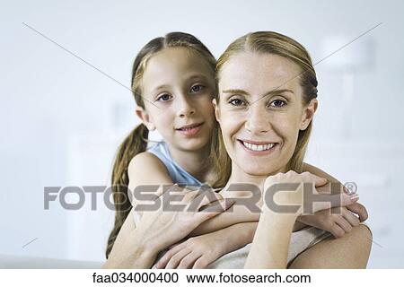 Stock Image - Mother and daughter embracing, both smiling at camera. Fotosearch