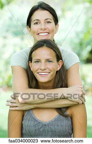Mother standing behind teenage daughter, embracing her, both smiling at camera, portrait View Large Photo Image Stock Image - Mother standing behind teenage daughter, embracing her, both smiling at camera, portrait. Fotosearch