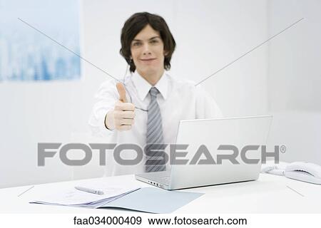Stock Photo - Office worker sitting at desk, making thumbs up sign at camera. Fotosearch