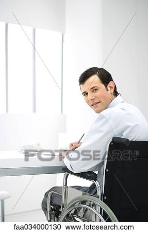 Professional man in wheelchair working at desk, smiling over shoulder at camera View Large Photo Image Stock Image - Professional man in wheelchair working at desk, smiling over shoulder at camera. Fotosearch