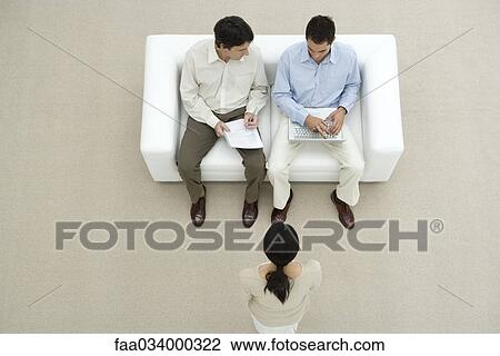 Professional men sitting on sofa, discussing document, woman standing before them, overhead view View Large Photo Image Stock Image - Professional men sitting on sofa, discussing document, woman standing before them, overhead view. Fotosearch