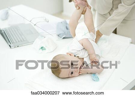 Stock Photo - Professional woman changing infant's diaper on desk, infant looking at camera. Fotosearch