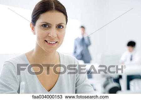 Professional woman smiling at camera, male colleagues in background View Large Photo Image Stock Image - Professional woman smiling at camera, male colleagues in background. Fotosearch