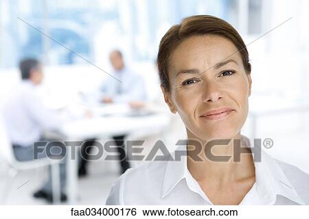 Professional woman smiling at camera, portrait, male colleagues working in background View Large Photo Image Stock Photograph - Professional woman smiling at camera, portrait, male colleagues working in background. Fotosearch