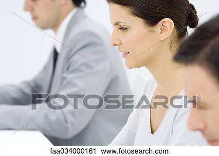 Stock Image - Professionals working, profile, focus on woman in center. Fotosearch