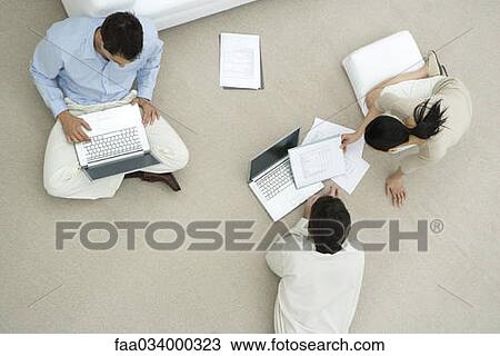 Stock Image - Professionals working together on floor, two discussing document, overhead view. Fotosearch