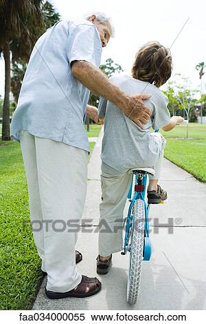 Stock Photography - Senior man helping his grandson learn to ride a bicycle. Fotosearch