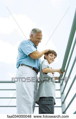 Stock Photo - Senior man with grandson on balcony, his hand on his head, both smiling. Fotosearch
