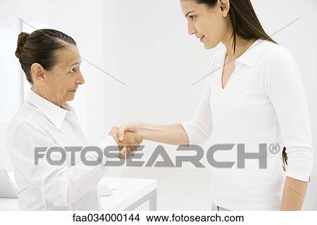 Picture - Senior woman shaking young woman's hand, side view. Fotosearch