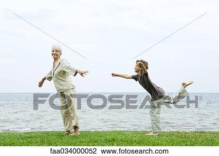 Stock Image - Senior woman stretches as grandson balances standing on one leg. Fotosearch