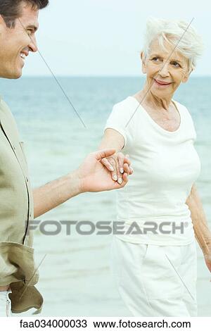 Senior woman walking hand in hand with adult son by water, smiling at each other View Large Photo Image Stock Image - Senior woman walking hand in hand with adult son by water, smiling at each other. Fotosearch