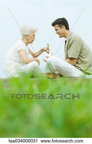 Senior woman with adult son, sitting in park sharing takeout food with chopsticks View Large Photo Image Stock Image - Senior woman with adult son, sitting in park sharing takeout food with chopsticks . Fotosearch