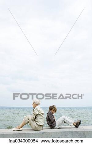 Picture - Senior woman with grandson, sitting back to back, not looking at each other. Fotosearch