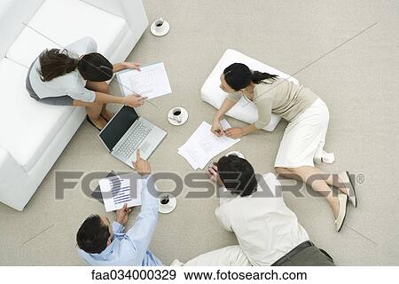 Stock Photo - Team of professionals discussing documents in casual work environment, overhead view. Fotosearch