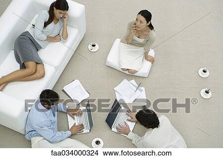 Picture - Team of professionals working together on floor, one woman napping on sofa, overhead view. Fotosearch