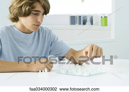 Stock Image - Teen boy sitting at table, playing chess. Fotosearch