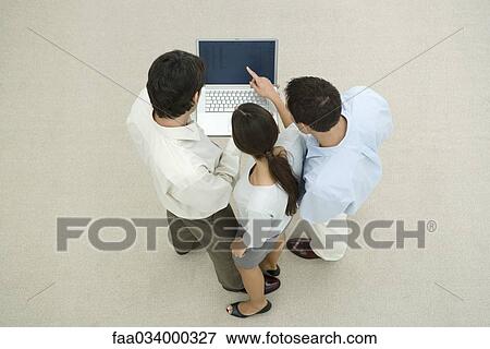 Stock Photo - Three professionals standing, looking at laptop computer together, high angle view. Fotosearch