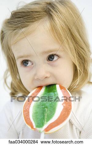 Picture - Toddler girl eating large lollipop, looking away. Fotosearch