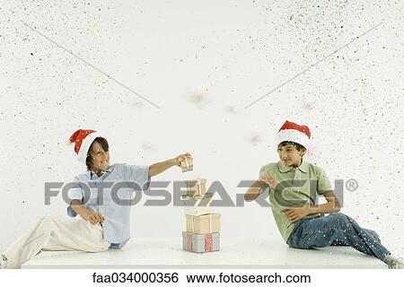 Two boys wearing Santa hats stacking presents, confetti falling around them View Large Photo Image Stock Photograph - Two boys wearing Santa hats stacking presents, confetti falling around them. Fotosearch
