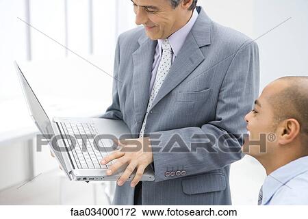 Stock Image - Two businessmen looking at laptop computer together, both smiling. Fotosearch