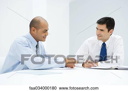 Two businessmen sitting at table, discussing document View Large Photo Image Stock Image - Two businessmen sitting at table, discussing document. Fotosearch