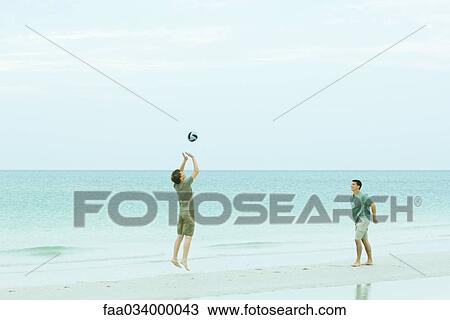 Stock Image - Two men playing volleyball on beach. Fotosearch