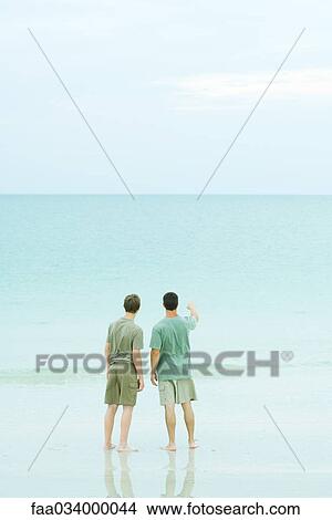 Picture - Two men standing on beach looking at the horizon. Fotosearch
