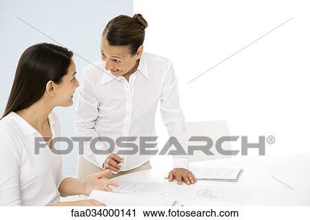 Two professional women discussing documents, smiling at each other View Large Photo Image Stock Image - Two professional women discussing documents, smiling at each other. Fotosearch