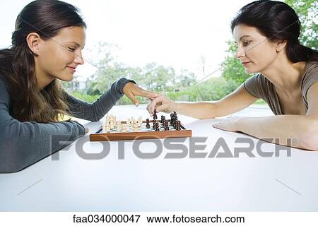 Stock Photo - Two women playing chess, one making a move, the other touching her hand. Fotosearch
