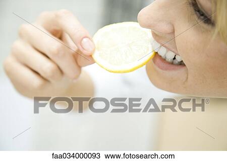 Stock Image - Woman biting into slice of lemon, smiling, close up. Fotosearch
