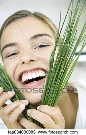 Stock Image - Woman holding chives up to face, smiling, laughing. Fotosearch