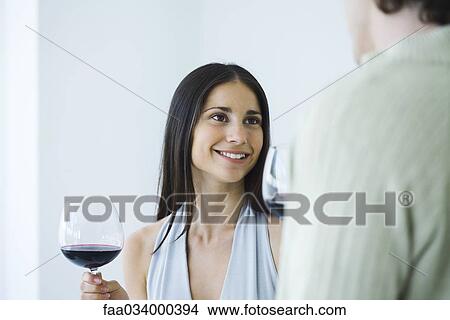 Woman holding glass of red wine and smiling at man, cropped view View Large Photo Image Picture - Woman holding glass of red wine and smiling at man, cropped view. Fotosearch
