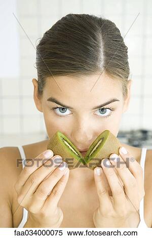 Woman holding halves of kiwi to her nose, looking at camera View Large Photo Image Stock Photography - Woman holding halves of kiwi to her nose, looking at camera. Fotosearch