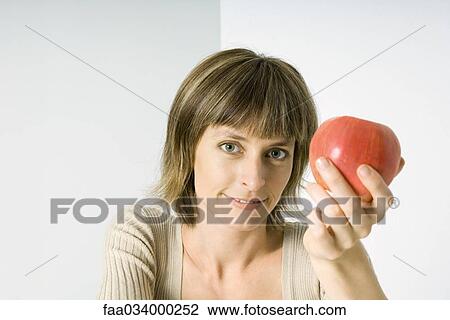 Woman holding red apple, smiling at camera View Large Photo Image Stock Image - Woman holding red apple, smiling at camera. Fotosearch