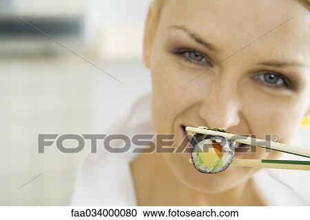 Stock Image - Woman holding sushi roll with chopsticks, smiling. Fotosearch