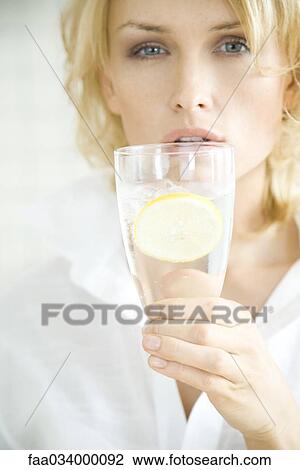 Stock Image - Woman holding up glass of water, looking at camera. Fotosearch